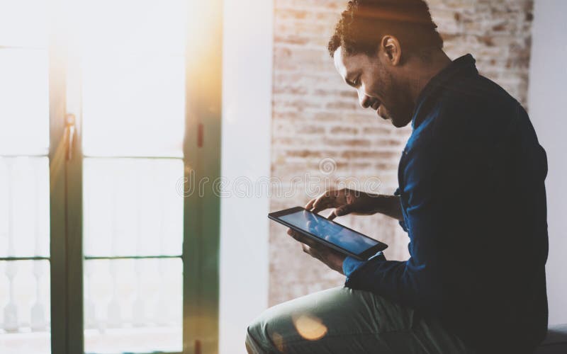 Het glimlachen jonge Afrikaanse Amerikaanse freelancer wat betreft het scherm digitale tablet terwijl thuis het werken in nieuw p royalty-vrije stock foto Het glimlachen jonge Afrikaanse Amerikaanse freelancer wat betreft het scherm digitale tablet terwijl thuis het werken in nieuw p royalty-vrije stock foto