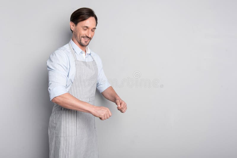 Het glimlachen mens het gesturing in een schort op een grijze achtergrond stock foto Het glimlachen mens het gesturing in een schort op een grijze achtergrond stock foto