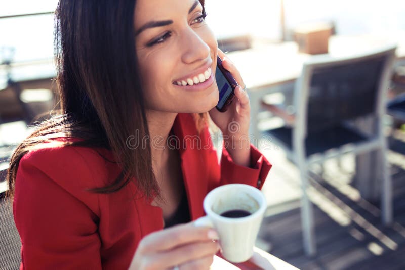 Het glimlachen van jonge vrouw het drinken koffie terwijl het texting met haar mobiele telefoon wodden lijst in het terras van ee stock foto Het glimlachen van jonge vrouw het drinken koffie terwijl het texting met haar mobiele telefoon wodden lijst in het terras van ee stock foto