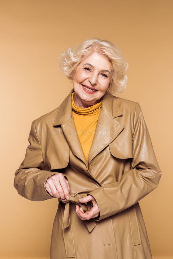 het glimlachen van modieuze hogere vrouwen bindende riem van leertrenchcoat stock afbeeldingen het glimlachen van modieuze hogere vrouwen bindende riem van leertrenchcoat stock afbeeldingen