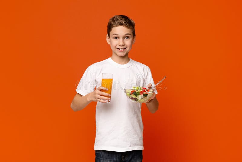 Het glimlachen van weinig jongen die plantaardig salade en jus d'orange eten stock afbeelding Het glimlachen van weinig jongen die plantaardig salade en jus d'orange eten stock afbeelding