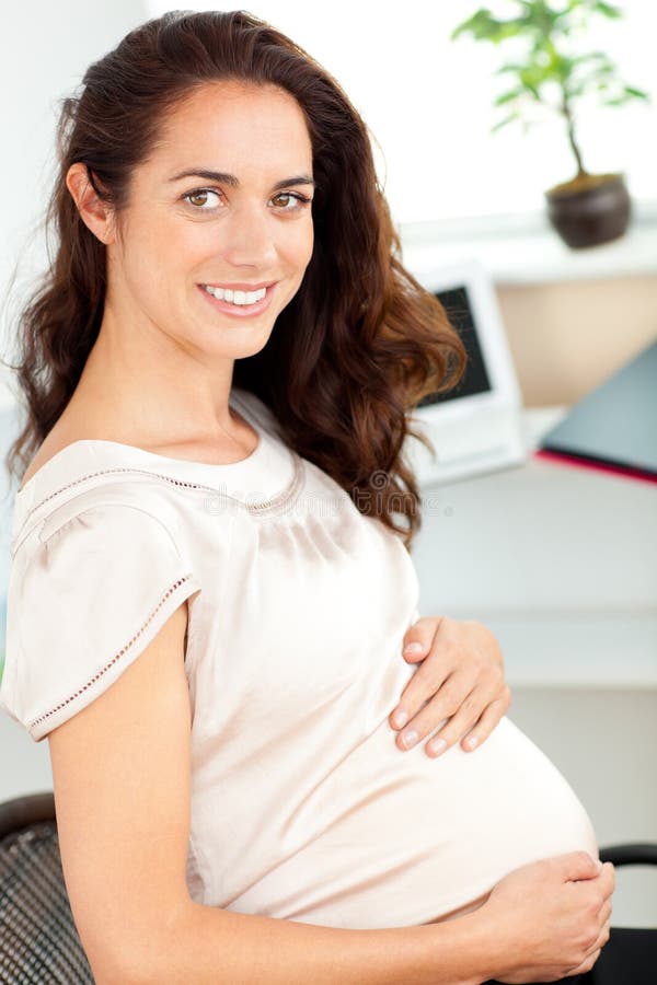 Pregnant businesswoman smiling at the camera sitting at her desk in her office. Pregnant businesswoman smiling at the camera sitting at her desk in her office