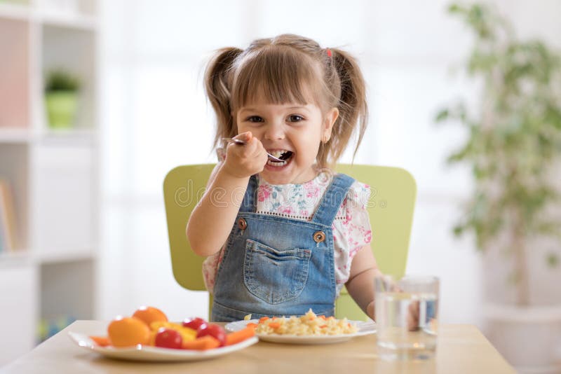 Het glimlachende peutermeisje eet thuis stock afbeelding Het glimlachende peutermeisje eet thuis stock afbeelding