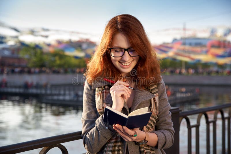 Het glimlachende vrolijke meisje maakt een nota in een notitieboekje, plannend hoe t stock foto Het glimlachende vrolijke meisje maakt een nota in een notitieboekje, plannend hoe t stock foto