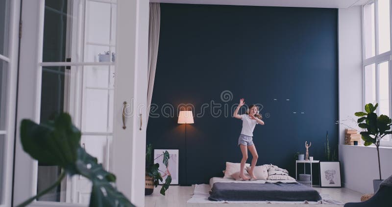 Het grappige leuke meisje in het draadloze hoofdtelefoons het dansen zingen met kam en heeft pret in vakantieochtend die op bed s stock video Het grappige leuke meisje in het draadloze hoofdtelefoons het dansen zingen met kam en heeft pret in vakantieochtend die op bed s stock video