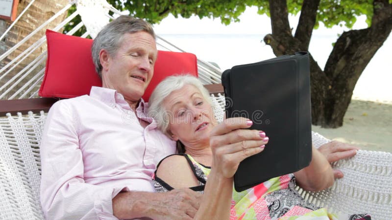Het hogere Paar Ontspannen in Strandhangmat die Digitale Tablet gebruiken