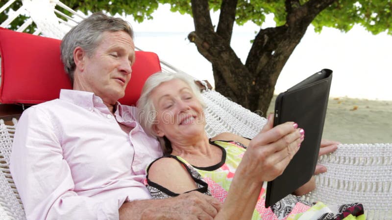 Het hogere Paar Ontspannen in Strandhangmat die Digitale Tablet gebruiken