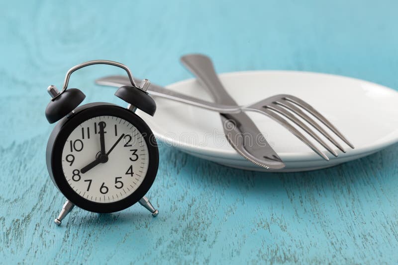 Clock with white plate, fork and knife, intermittent fasting, diet, weight loss concept on blue wooden table. Clock with white plate, fork and knife, intermittent fasting, diet, weight loss concept on blue wooden table