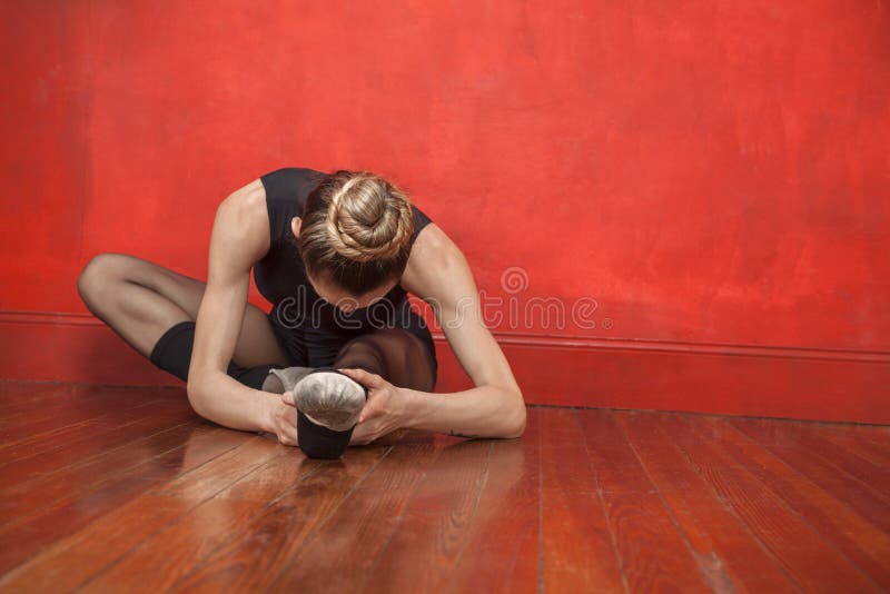 Young ballerina stretching her legs on hardwood floor in studio. Young ballerina stretching her legs on hardwood floor in studio