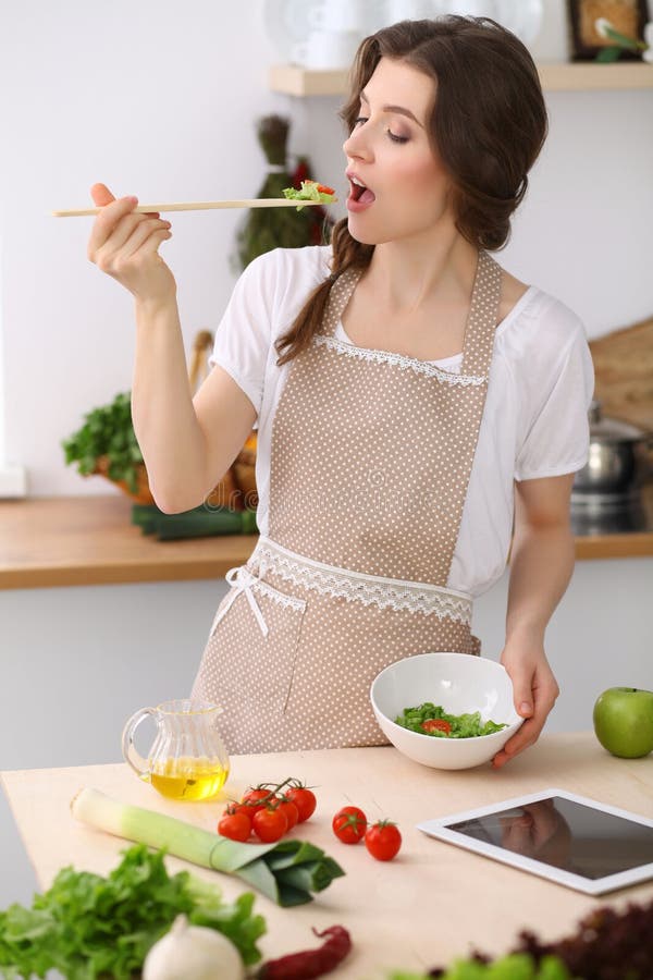 Het jonge donkerbruine vrouw koken in keuken Huisvrouw die houten lepel in haar hand houden Voedsel en gezondheidsconcept royalty-vrije stock foto Het jonge donkerbruine vrouw koken in keuken Huisvrouw die houten lepel in haar hand houden Voedsel en gezondheidsconcept royalty-vrije stock foto