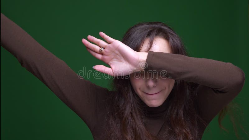 Het jonge donkerbruine vrouwelijke student synchroniseren die gelukkig en tevreden op groene achtergrond zijn