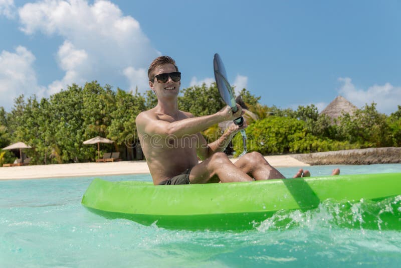 Het jonge gelukkige mens kayaking op een tropisch eiland in de Maldiven Duidelijk Blauw Water stock afbeeldingen Het jonge gelukkige mens kayaking op een tropisch eiland in de Maldiven Duidelijk Blauw Water stock afbeeldingen