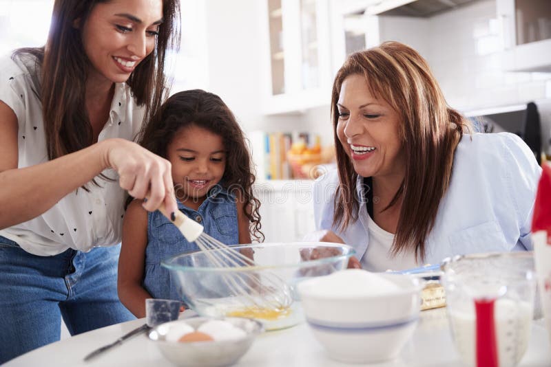 Het jonge meisje die een cake in de keuken met haar mum en grootmoeder maken, sluit omhoog stock afbeelding Het jonge meisje die een cake in de keuken met haar mum en grootmoeder maken, sluit omhoog stock afbeelding