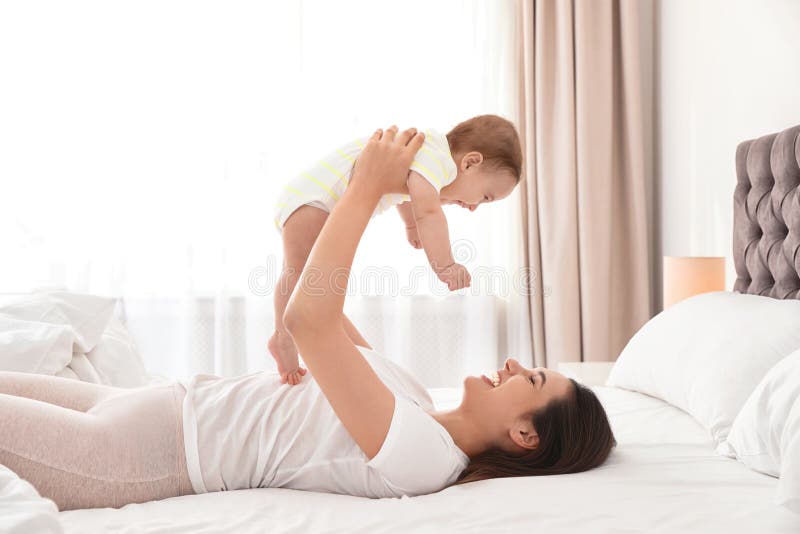 Het jonge moeder spelen met haar leuke baby op bed royalty-vrije stock afbeelding Het jonge moeder spelen met haar leuke baby op bed royalty-vrije stock afbeelding