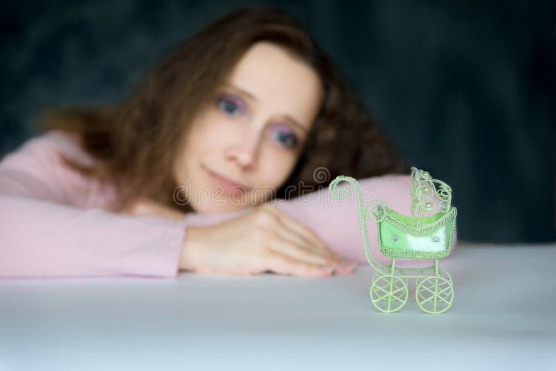 Het jonge mooie meisje bekijkt hopelijk een kinderwagenstuk speelgoed De wandelwagen in de voorgrond, een vrouw in het vage ondui royalty-vrije stock foto's Het jonge mooie meisje bekijkt hopelijk een kinderwagenstuk speelgoed De wandelwagen in de voorgrond, een vrouw in het vage ondui royalty-vrije stock foto's