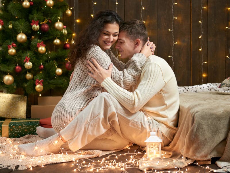 Het jonge paar zit op vloer in donker houten binnenland met lichten Romantisch avond en liefdeconcept De vakantie van het nieuwja stock foto's Het jonge paar zit op vloer in donker houten binnenland met lichten Romantisch avond en liefdeconcept De vakantie van het nieuwja stock foto's