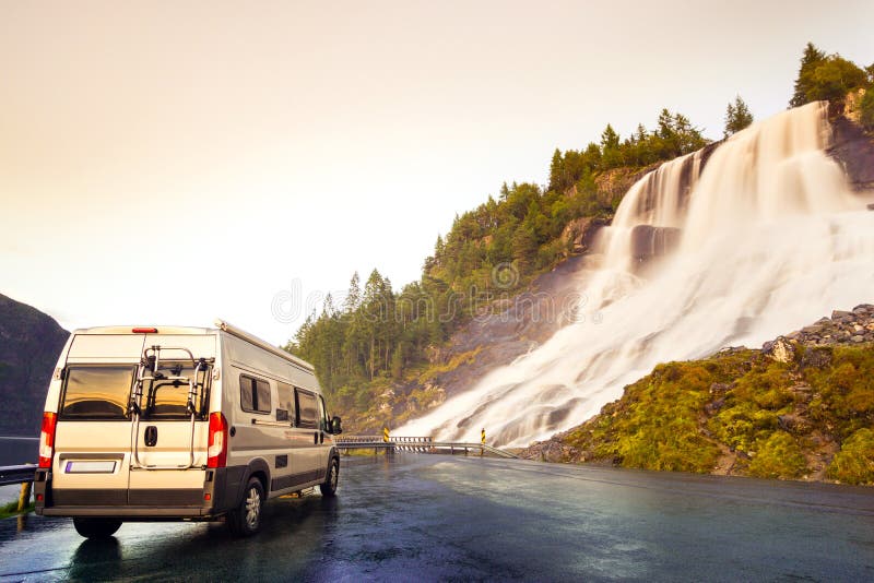 Het kamperen bestelwagen bij mooie reusachtige waterval Verbazende cataract bij weg in zonsonderganglicht noorwegen stock foto's Het kamperen bestelwagen bij mooie reusachtige waterval Verbazende cataract bij weg in zonsonderganglicht noorwegen stock foto's