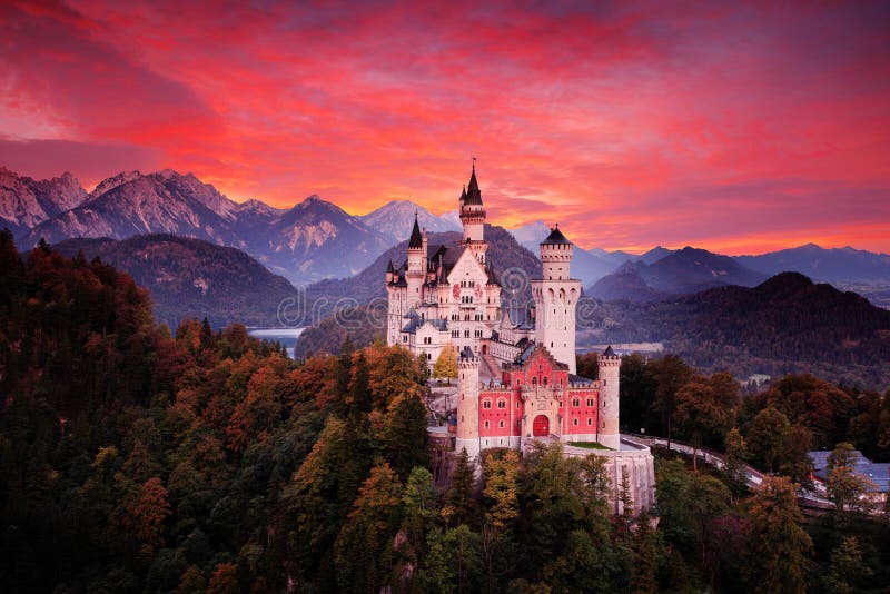 Het kasteel van het Neuschwansteinsprookje Mooie zonsondergangmening van de bloedige wolken met de herfstkleuren in bomen, scheme