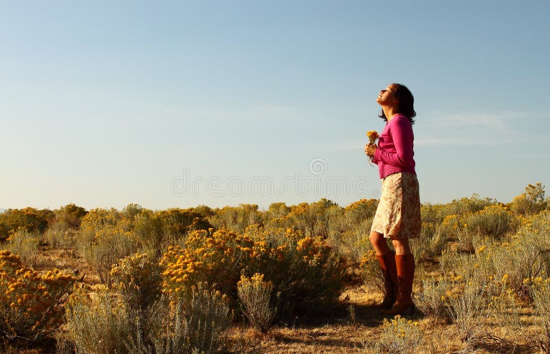 A young woman standing in a desert field with eyes closed in reverance and face towards the sun. A young woman standing in a desert field with eyes closed in reverance and face towards the sun.