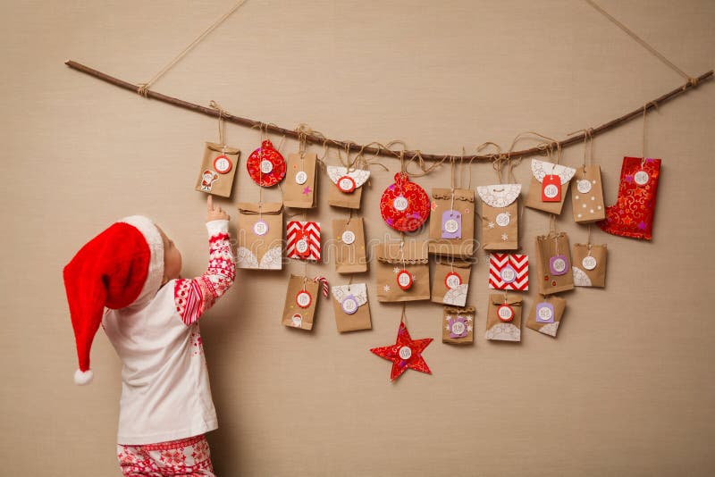 Het kind bekijkt de komstkalender Het babymeisje in een Kerstmishoed en pyjama's toont op eerste gift stock afbeeldingen Het kind bekijkt de komstkalender Het babymeisje in een Kerstmishoed en pyjama's toont op eerste gift stock afbeeldingen