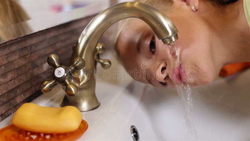 Het kind drinkt water van de badkamerstapkraan