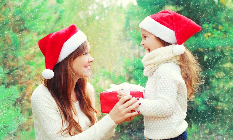 Het kind en de moeder van de Kerstmisfamilie in santa rode hoed met doosgift over boom stock afbeelding Het kind en de moeder van de Kerstmisfamilie in santa rode hoed met doosgift over boom stock afbeelding