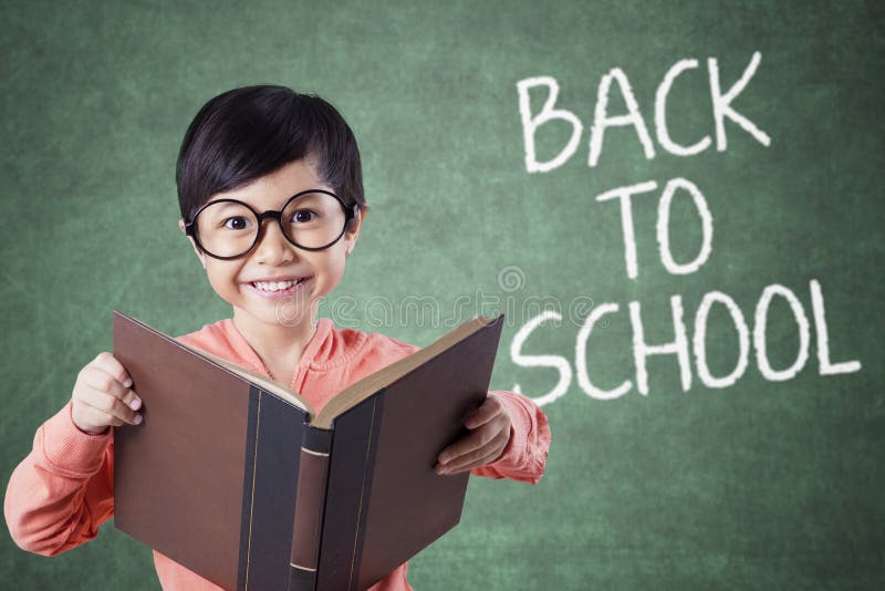 Het kind houdt boek met terug naar schooltekst in klasse stock afbeeldingen Het kind houdt boek met terug naar schooltekst in klasse stock afbeeldingen