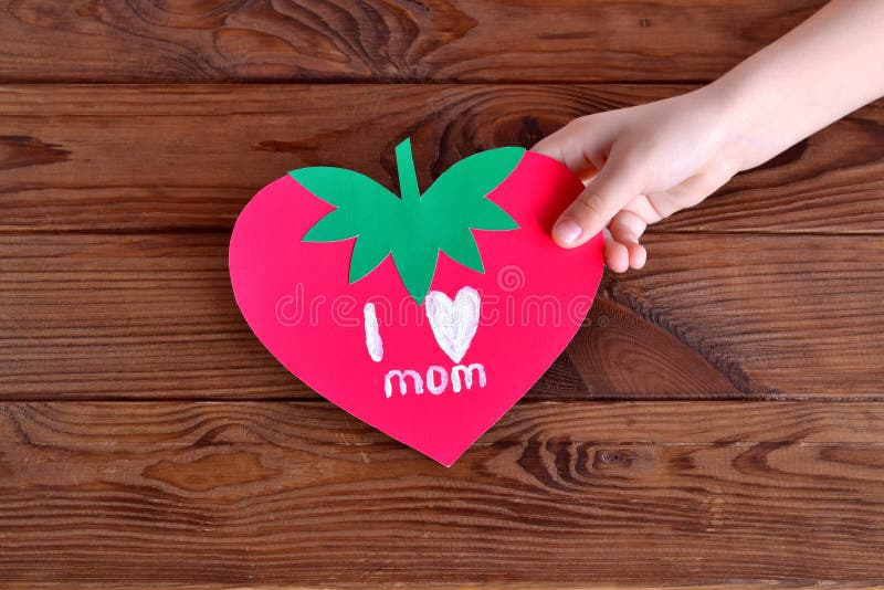 Het kind houdt een kaart in zijn hand Document kaartaardbei Groetkaart mother& x27; s dag Originele jonge geitjesambachten stock foto Het kind houdt een kaart in zijn hand Document kaartaardbei Groetkaart mother& x27; s dag Originele jonge geitjesambachten stock foto