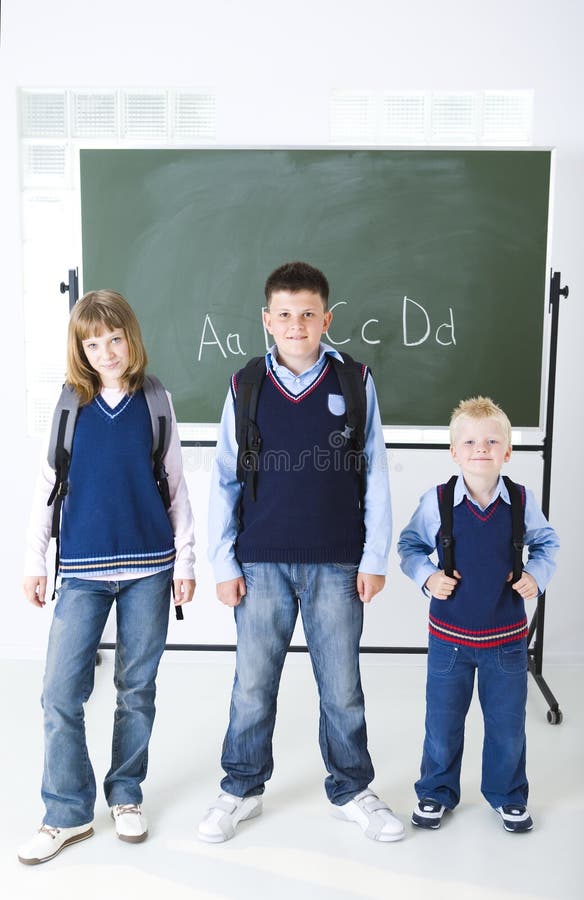 Three schoolchildren standing in front of chalkboard. They looking at camera. Three schoolchildren standing in front of chalkboard. They looking at camera.