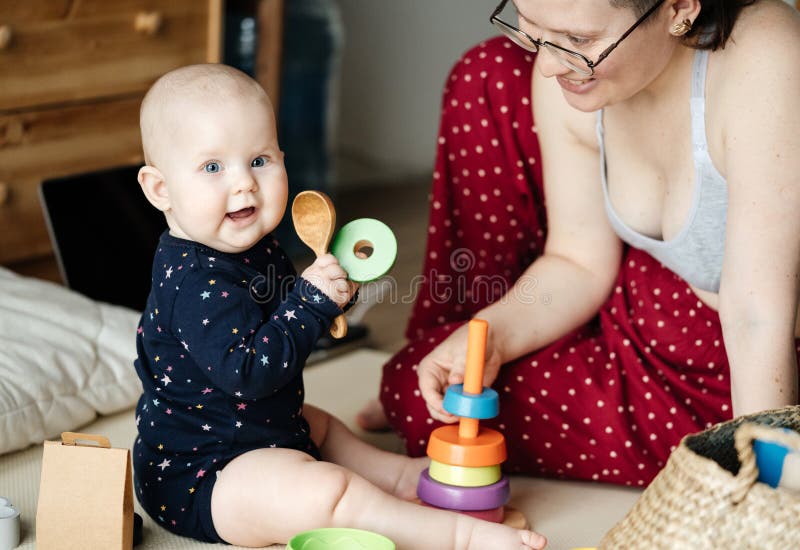 Het kleine kind zit op de vloer die een houten lepel in zijn handen houden en gelukkig met zijn moeder binnen spelen stock foto's Het kleine kind zit op de vloer die een houten lepel in zijn handen houden en gelukkig met zijn moeder binnen spelen stock foto's