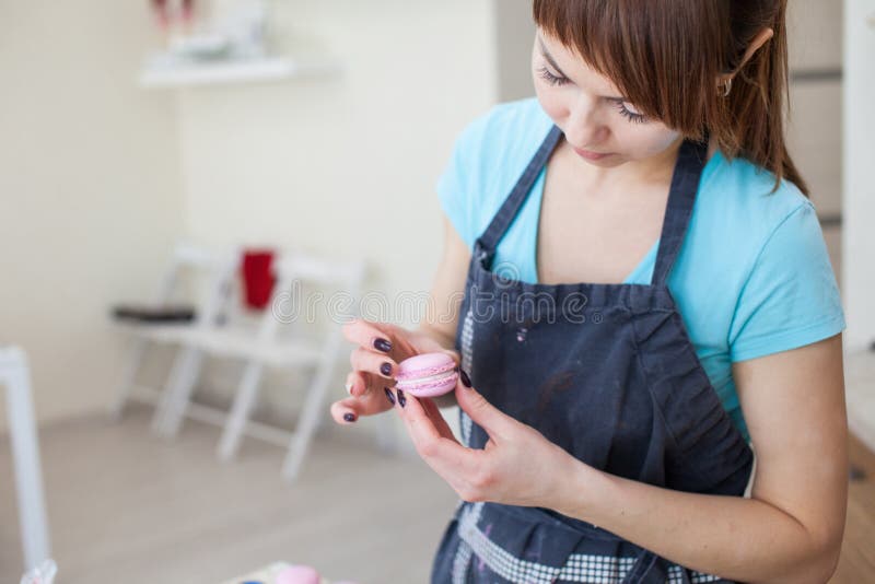 Het koken, voedsel en het bakken concept - chef-kok die met banketbakkerijzak room het vullen drukken aan macaronsshells bij pati stock afbeeldingen Het koken, voedsel en het bakken concept - chef-kok die met banketbakkerijzak room het vullen drukken aan macaronsshells bij pati stock afbeeldingen