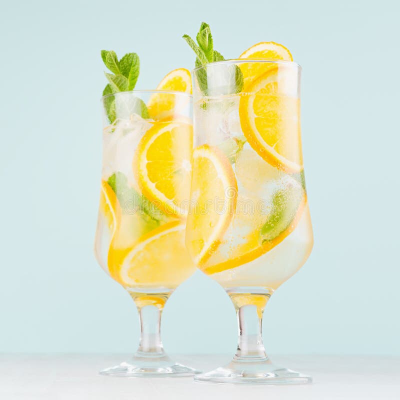 Het koude tropische sinaasappelensap misted binnen wijnglas met gesneden fruit, munt, ijsblokjes op pastelkleur zachte blauwe ach stock foto's Het koude tropische sinaasappelensap misted binnen wijnglas met gesneden fruit, munt, ijsblokjes op pastelkleur zachte blauwe ach stock foto's