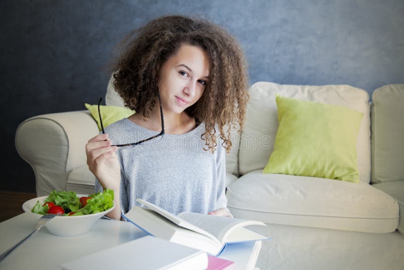 Het krullende boek van de het meisjeslezing van de haartiener en het eten van salade stock afbeeldingen Het krullende boek van de het meisjeslezing van de haartiener en het eten van salade stock afbeeldingen