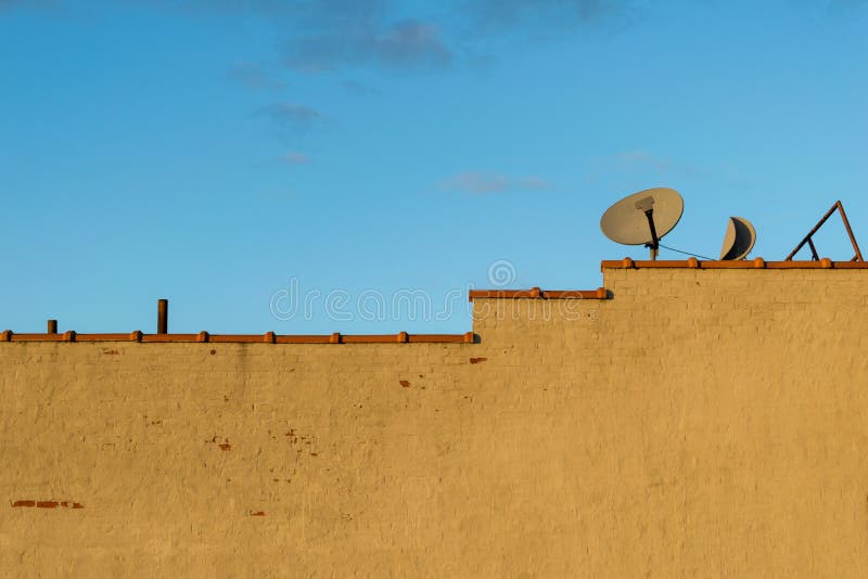 Het lege geschilderde bakstenen muur en terracottakleidakwerk betegelt dakspanen, en een paar oude satelliettv-ontvangersschotels stock foto's Het lege geschilderde bakstenen muur en terracottakleidakwerk betegelt dakspanen, en een paar oude satelliettv-ontvangersschotels stock foto's