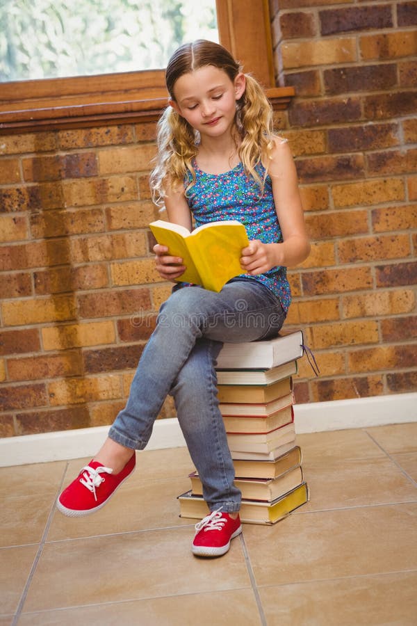 Full length of cute little girl reading book in the library. Full length of cute little girl reading book in the library