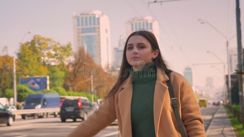 Het leuke Kaukasische meisje met bruine ogen en lang aardig haar probeert de achterstand in te lopen auto terwijl status dichtbij