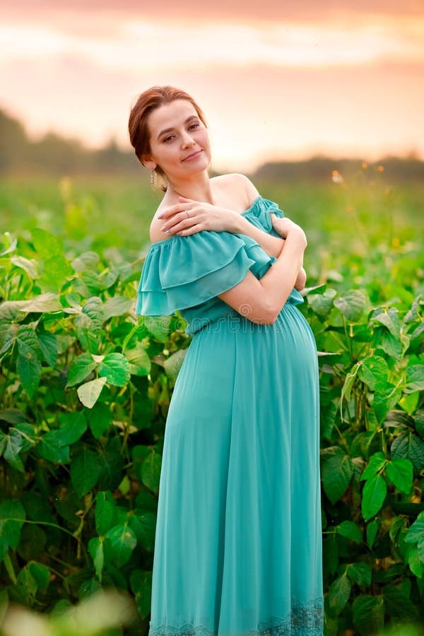 Het leuke zwangere meisje in een groene kleding bevindt zich op een gebied bij zonsondergang stock fotografie Het leuke zwangere meisje in een groene kleding bevindt zich op een gebied bij zonsondergang stock fotografie