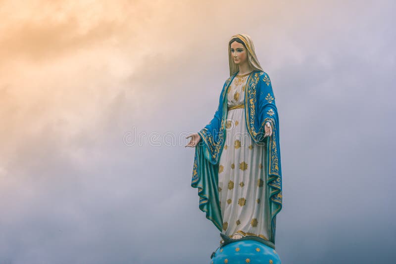 Het maagdelijke standbeeld van Mary bij Katholieke kerk met zonlicht op bewolkte dagachtergrond
