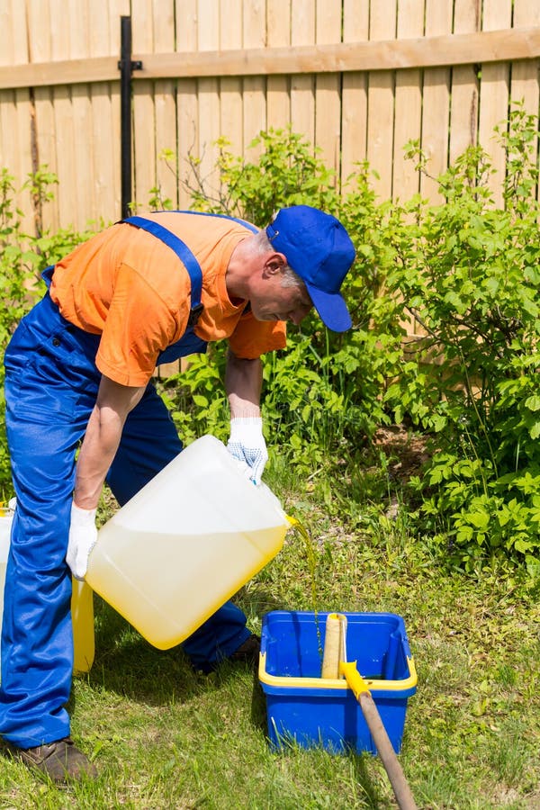 Het manusje van alles in het blauwe eenvormig werken giet gele antiseptische verf van kan royalty-vrije stock afbeelding Het manusje van alles in het blauwe eenvormig werken giet gele antiseptische verf van kan royalty-vrije stock afbeelding