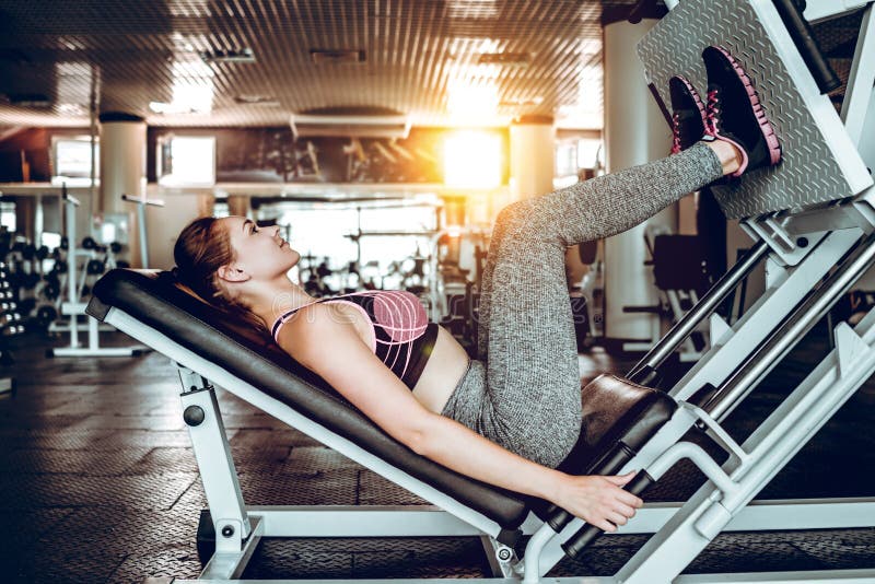 Het meisje is bezig geweest met geschiktheidstraining met de pers van het simulatorbeen bij gymnastiek royalty-vrije stock fotografie Het meisje is bezig geweest met geschiktheidstraining met de pers van het simulatorbeen bij gymnastiek royalty-vrije stock fotografie