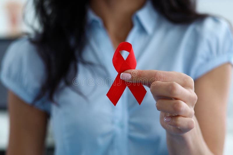 Girl holding breast cancer emblem in solidarity. Young woman in white blouse holds sign from red ribbon, symbol fight woman with breast cancer. Emotional support for women with cancer. Girl holding breast cancer emblem in solidarity. Young woman in white blouse holds sign from red ribbon, symbol fight woman with breast cancer. Emotional support for women with cancer.