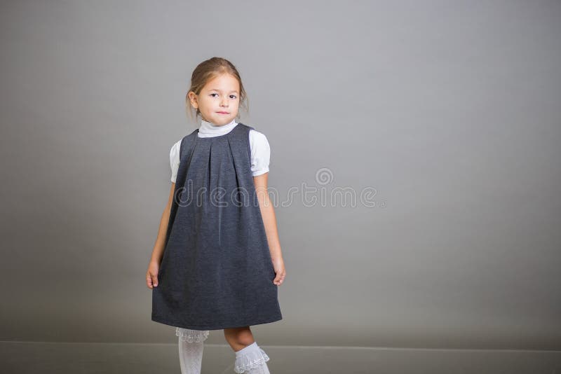 Het meisje de eerste nivelleermachine in een eenvormige school - stellen grijze sundress en een witte blouse op een grijze achter royalty-vrije stock foto's Het meisje de eerste nivelleermachine in een eenvormige school - stellen grijze sundress en een witte blouse op een grijze achter royalty-vrije stock foto's