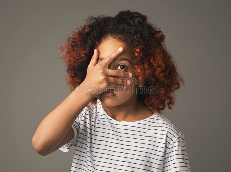 Het meisje die van het Afrojonge geitje hoewel vingers op grijze achtergrond gluren royalty-vrije stock foto Het meisje die van het Afrojonge geitje hoewel vingers op grijze achtergrond gluren royalty-vrije stock foto