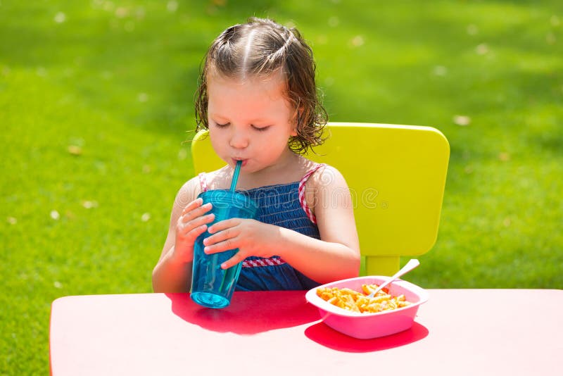 Het meisje die van het peuterjonge geitje etend deegwaren in tuin drinken royalty-vrije stock foto Het meisje die van het peuterjonge geitje etend deegwaren in tuin drinken royalty-vrije stock foto