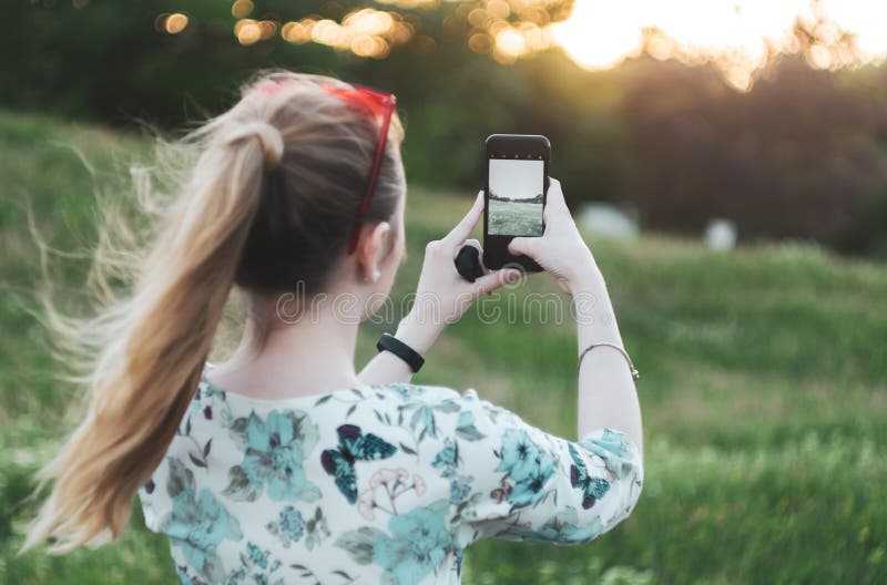 Het meisje fotografeert de zonsondergang op de telefoon achtermening stock foto's Het meisje fotografeert de zonsondergang op de telefoon achtermening stock foto's
