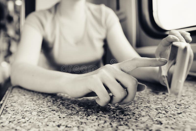 Het meisje in haar handen houdt een mobiele telefoon en port haar vinger in de reis door trein en trein in de auto stock afbeelding Het meisje in haar handen houdt een mobiele telefoon en port haar vinger in de reis door trein en trein in de auto stock afbeelding