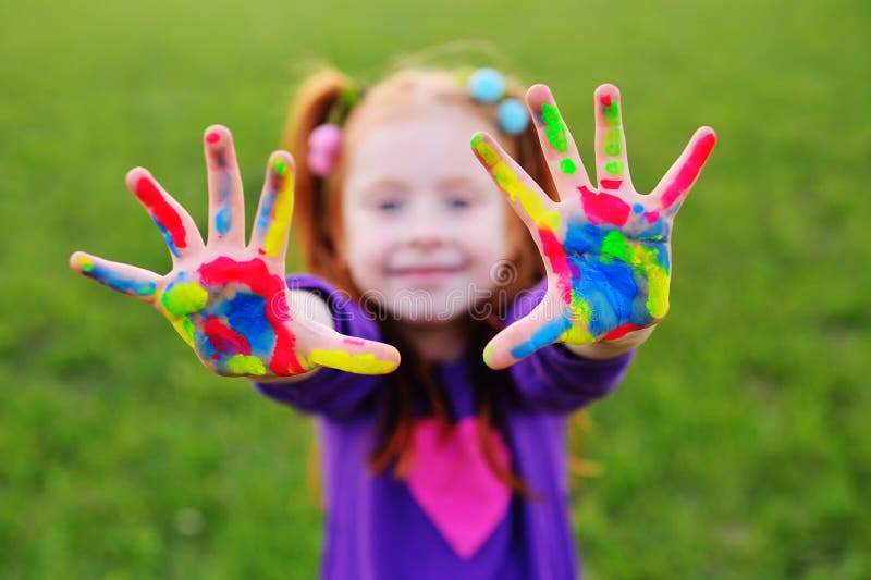 Het meisje met rood haar toont haar handen vuil met multicolored verven en glimlacht royalty-vrije stock fotografie Het meisje met rood haar toont haar handen vuil met multicolored verven en glimlacht royalty-vrije stock fotografie