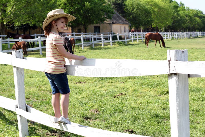 Little girl with cowboy hat standing on corral and watching horses. Little girl with cowboy hat standing on corral and watching horses