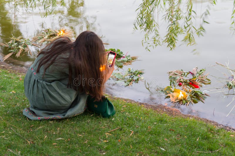 Het meisje neemt beelden van een kroon van bloemen in het meer, uitvoerend de traditionele rite van de vakantie van Ivan Kupala stock foto's Het meisje neemt beelden van een kroon van bloemen in het meer, uitvoerend de traditionele rite van de vakantie van Ivan Kupala stock foto's
