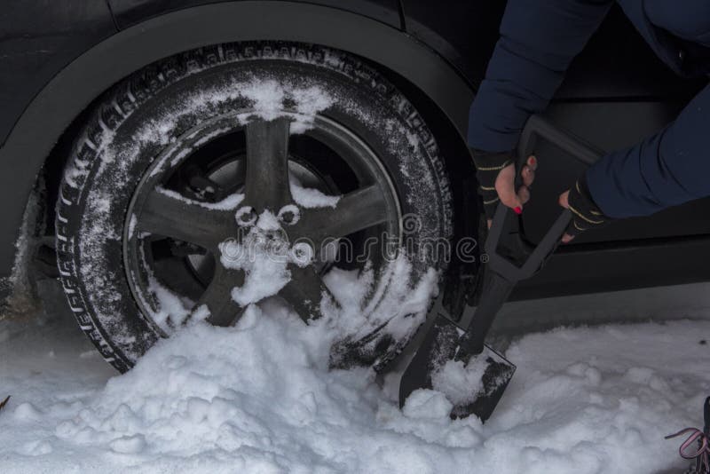Het meisje verwijdert sneeuw uit het achterwiel van haar auto, royalty-vrije stock foto Het meisje verwijdert sneeuw uit het achterwiel van haar auto, royalty-vrije stock foto